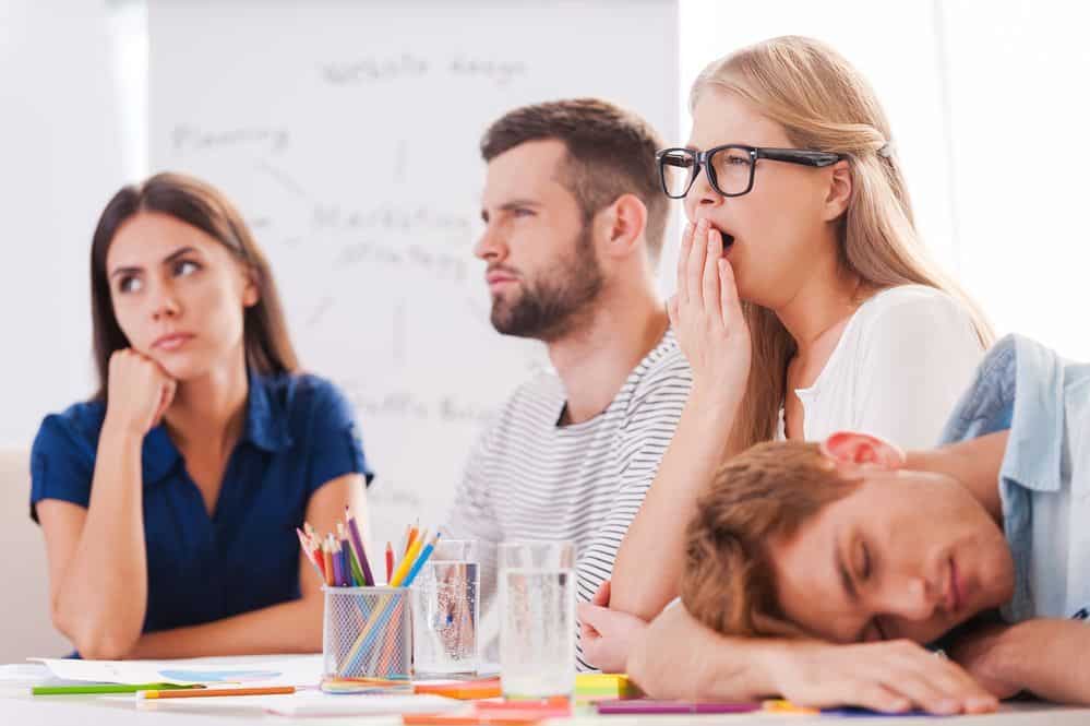 Boring presentation. Group of young business people in smart casual wear looking bored while sitting together at the table and looking away