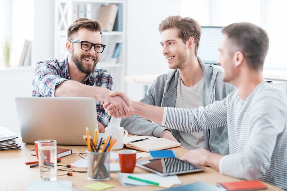 Sealing a deal. Business people shaking hands while sitting at the desk in office
